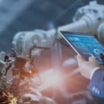 A man in a suit is using a tablet in front of a machine.